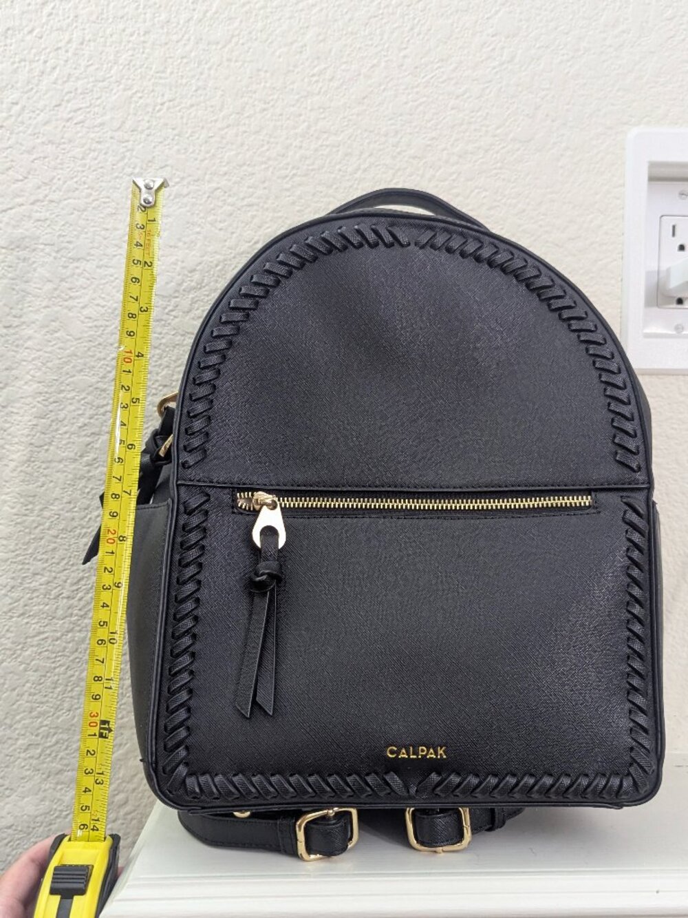 - Black saffiano faux leather CALPAK backpack has a rounded silhouette with brai